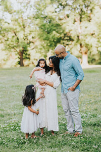 Family with two young girls looks at baby during photo session in Spring