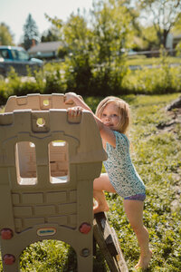 toddler girls looks at camera as she climbs a small ladder to the top of a slide while wearing a floral bathing suit