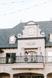 Bride and groom kiss on outdoor balcony on their wedding day