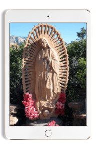 Ipad with image of tan  Mother Mary statue in a garden with pink flowers