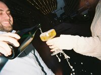A playful and celebratory engagement moment in downtown Dallas, featuring a couple popping champagne and toasting against the city lights.

