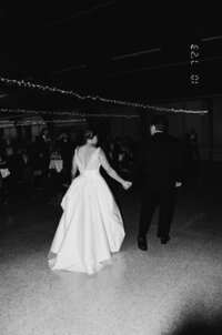 Black and white film image of a bride and groom walking at their wedding reception.