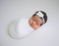 Lovely baby girl wrapped in white and sleeping on a white sheet. Newborn session by E. Benecki Photography.