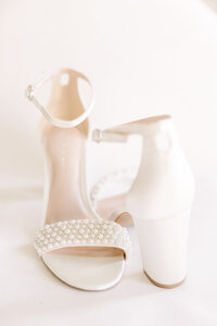 Elegant white bridal shoes with pearl embellishments, beautifully arranged against a soft, light background.