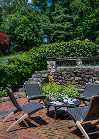 Original garden wall with climbing greens beside modern foldable furniture on an aged brick patio, blending historic charm with contemporary design. 