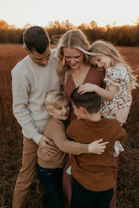 Photo of a beautiful family with three young kids giving a group hug during golden hour in the fall at their family photoshoot in Bloomington Indiana.