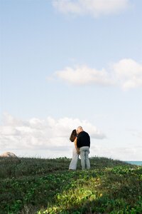 Elopement Photography, couple standing together on a large hill with the sky stretched out above them