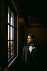 Groom standing in the light of a window, dressed in his wedding day attire