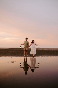 Bride and groom holding lanterns by lake at dusk during engagement session