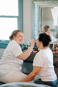A person sitting down and doing someone's makeup 