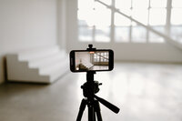 Tripod holding a phone that is recording a large open space with stunning open windows.