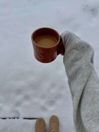 woman wearing gray sweatshirt holding cup of coffee outside in snow