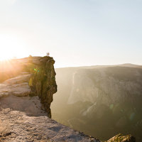The sun sets at Taft Point in Yosemite National park as the couple stands on a cliff in the far distance.