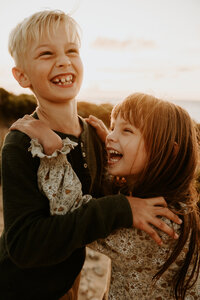 Brother and sister laugh and hug during sunset photography session