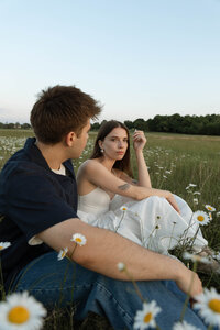 Couple sitting in a field during golden hour, captured in romantic film-inspired tones.