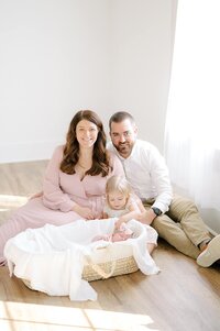 A family wearing pink poses  behind a baby in a bassinet during their newborn studio session