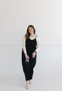 Tia Quirk wearing a black jumper and posing in front of a white background with her professional camera