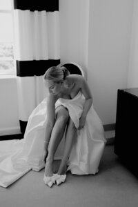 Bride adjusting her wedding shoes in a hotel room.