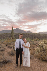 Couple smiles in the desert at the sun sets behind them