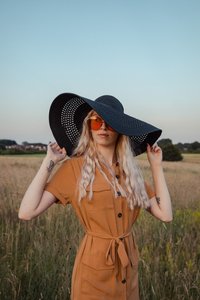 Amber in a field at golden hour wearing a black straw hat and round orange sunglasses