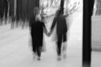 Black and white blurry photo of couple pictured from behind holding hands outdoors.