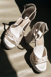 Elegant white bridal sandals with crystal embellishments casting dramatic shadows on a light surface, perfect for luxury wedding shoe detail photography.
