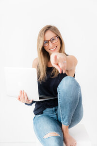 women with blue shirt and jeans with laptop pointing at screen