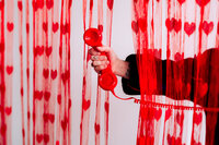 Woman in red tulle and heels posing between hanging streamers – custom creative portrait session by Mewphotovideo