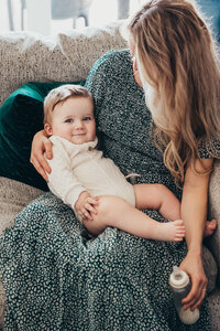 A sweet baby boy lays on his mother's lap and smiles at the camera during their in-home family session with Christine Dammann