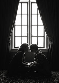gay couple lean in for a kiss while sitting in front of large window at dover hall in richmond, va