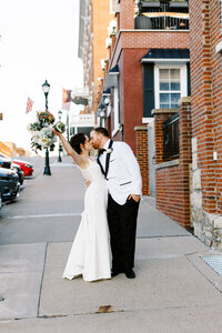 Newlyweds kissing on the street of Red Wing while the bride hold her gorgeous bouquet up high. Captured by Minnesota wedding photographer.