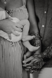 Close up of couple holding hands and baby's legs are in frame