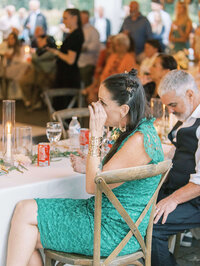 A guest dries their eyes at a wedding reception in a chair rental chair, representing ffordable & luxury event rentals.
