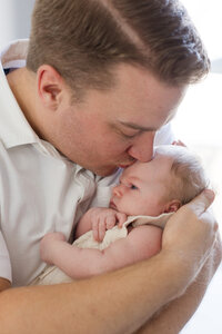 Dad kissing baby girl's forehead and cradling her in his arms during an in home shoot in Charlotte NC