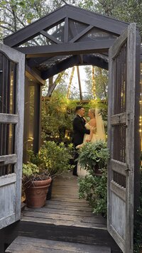 Twin Oaks Garden Estate wedding photo, romantic outdoor garden wedding San Marcos, Bride and groom under rustic wood arch, San Diego wedding content creator, luxury garden venue SoCal