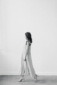 Woman stands looking over window with casual smling in white silk top with jeans and black stiletto shoes