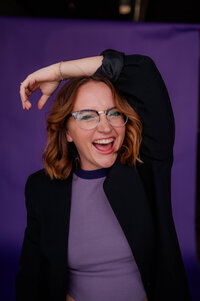 Rachel Hahn, owner of Rachel B Photography, poses in front of purple backdrop.