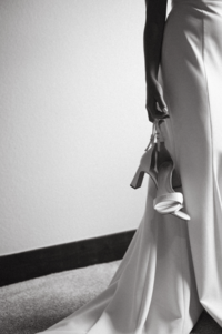 Bride getting ready in her wedding dress and holding her designer shoes in a bridal suite in Brooklyn, New York.