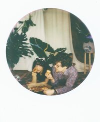 Polaroid photo of an engaged couple sharing pizza on the floor of a styled indoor set with tropical leaves and disco balls — captured by a film wedding photographer during an engagement session.