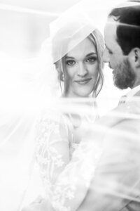 Bride wrapping her arms around the groom from behind in a black and white portrait, capturing an intimate and timeless moment of love and connection.