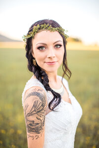 Fair skinned bride with tattoo on her arm and a boho hairpiece looks at the camera