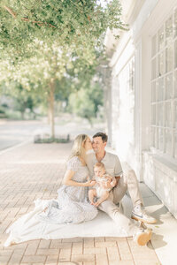 Family of three sitting closely on a soft blanket near a historic brick wall during a Kansas City family photography session.