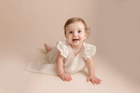 Eight month old baby girl on cream backdrop smiling on her tummy