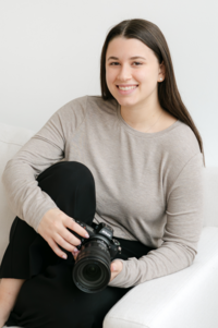 Ephe sits on a white couch with her leg near her chest and holds her Nikon camera.