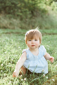 1 year old baby girl sits in the grass