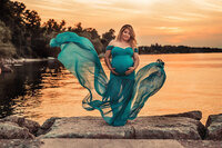 pregnant mom in blue flowy dress in front of sunset by the lake