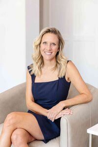 A high-end interior designer in Frisco sitting on an elegant white couch, wearing a navy blue dress.