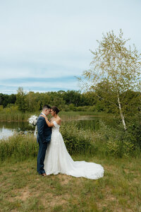 bride and groom standing together at a pond with trees in the background