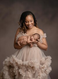 New mom holding her baby boy and amazed by his beauty. She is wearing a couture gown that Jenni Nikki provides in her client closet.
