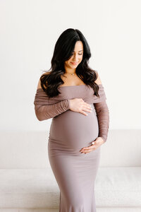 Expecting mom in purple dress holding baby and looking down during Indianapolis studio maternity photos